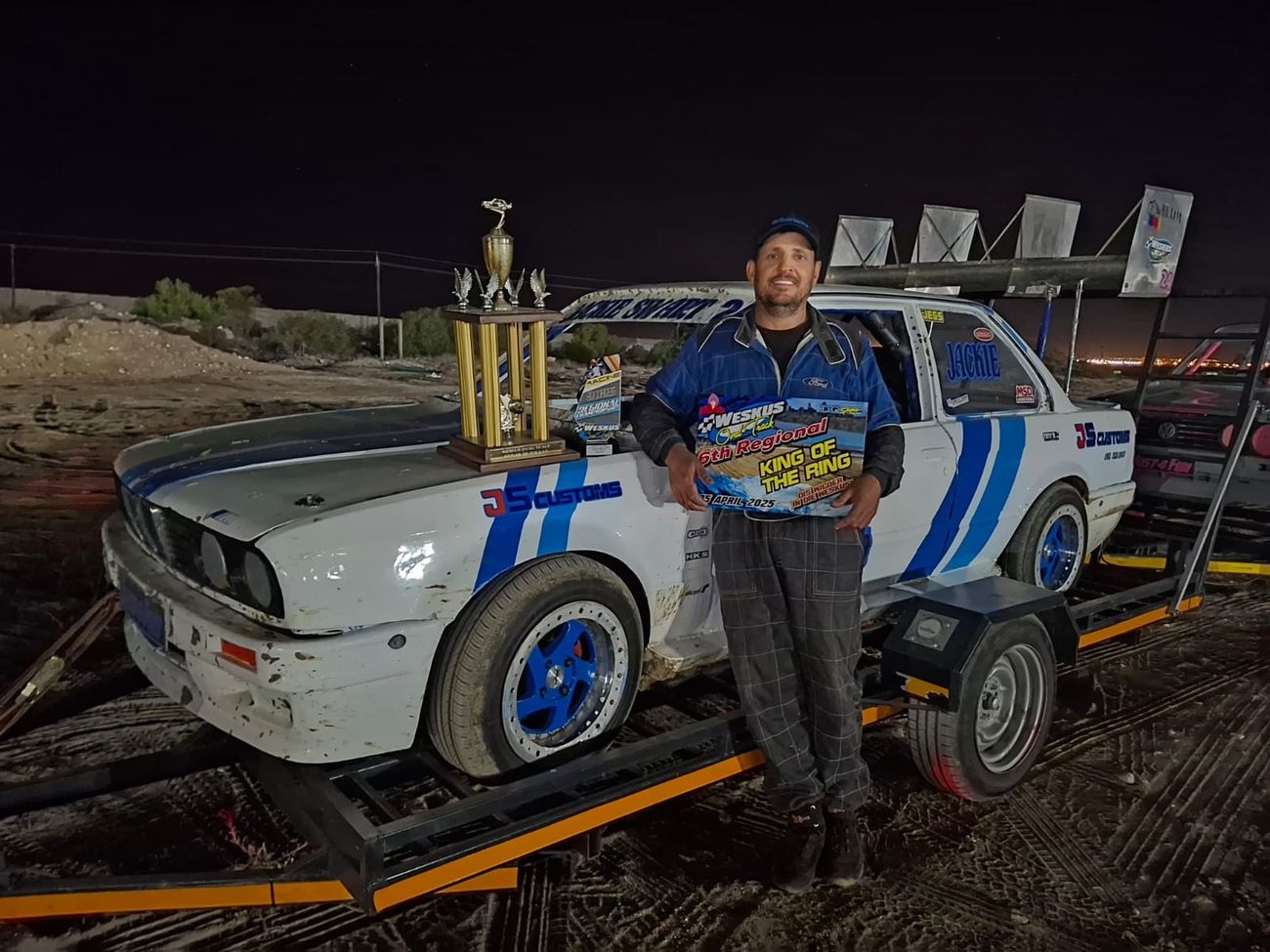 Jackie holding the King of the Ring trophy next to his white BMW E30 stock car